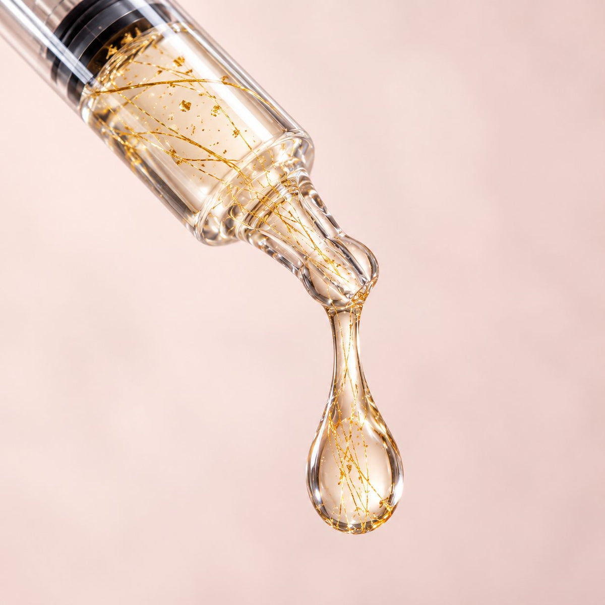 Goccia di siero con fili d’oro che scende dal dosatore